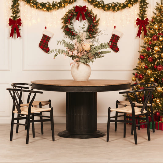 Round wooden dining table with black base and four chairs in a room with white paneled walls.