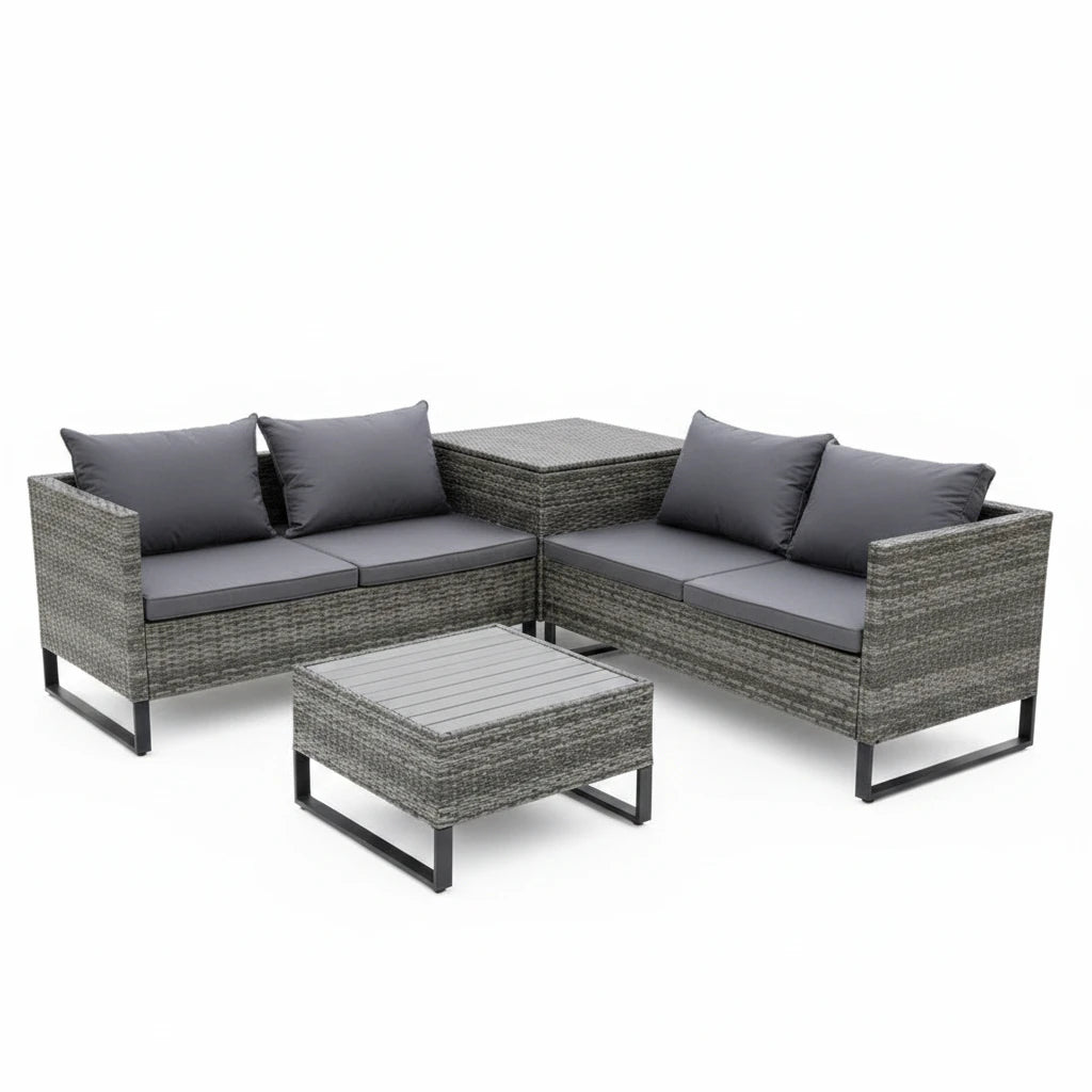 A 4-piece outdoor patio conversation set made of gray wicker with gray cushions, including a 3-seat sofa, a 2-seat sofa, a square coffee table, and a matching side table, arranged on a stone patio in a lush garden setting.